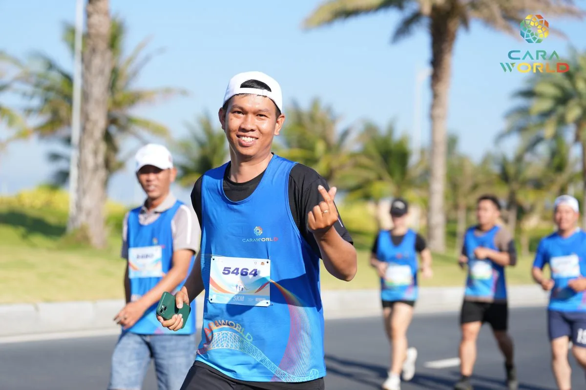 Vận động viên nam số 5464 mỉm cười giơ tay chào trên đại lộ cọ dừa CaraWorld Cara Run 2026